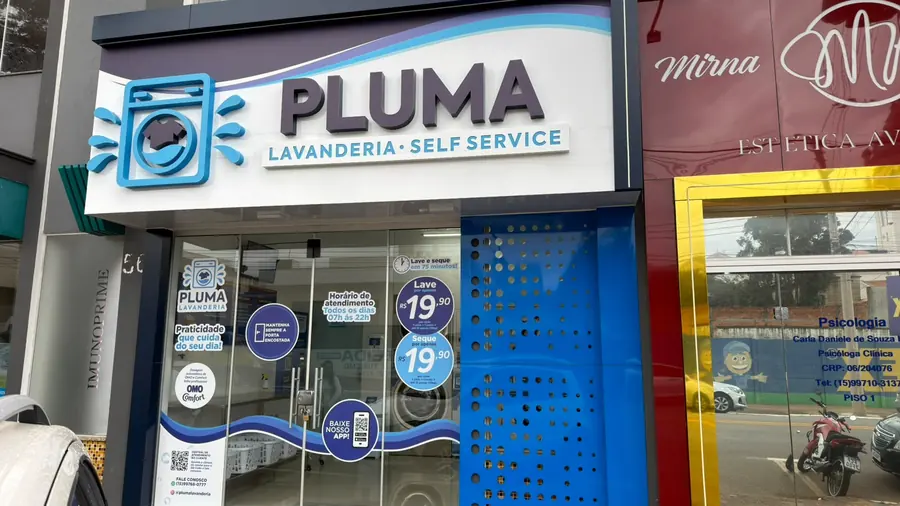 Letreiro da Pluma Lavanderia Self Service em Itararé, em branco e azul, sobre a entrada da loja na Rua São Pedro.